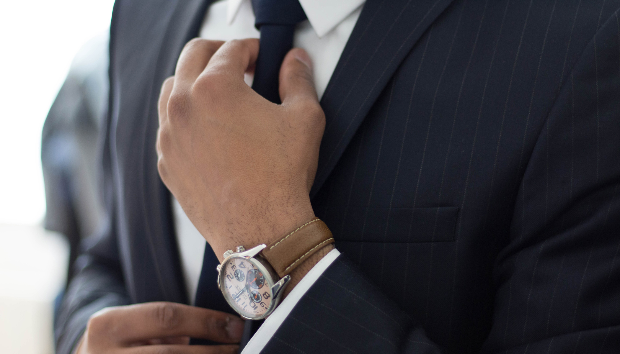 A close view of a pinstripe suit sleeve and tie being adjusted