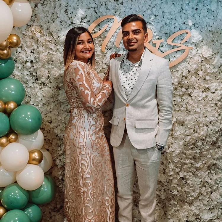 A couple at a celebration, him in a pale linen suit, her in an embroidered gown